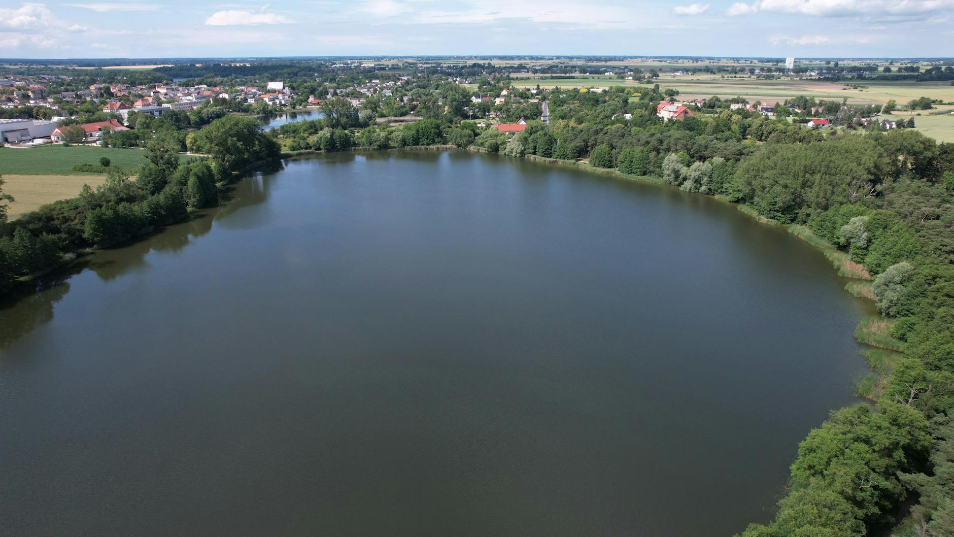 Grafika przedstawiająca planowany wygląd zrewitalizowanego stawu w Imielinie z terenami zielonymi i ścieżkami.
