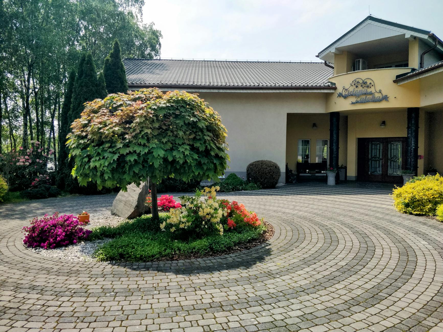 Zielone gałązki i kwiaty symbolizujące Zielone Świątki, z widokiem na imieliński krajobraz w tle.